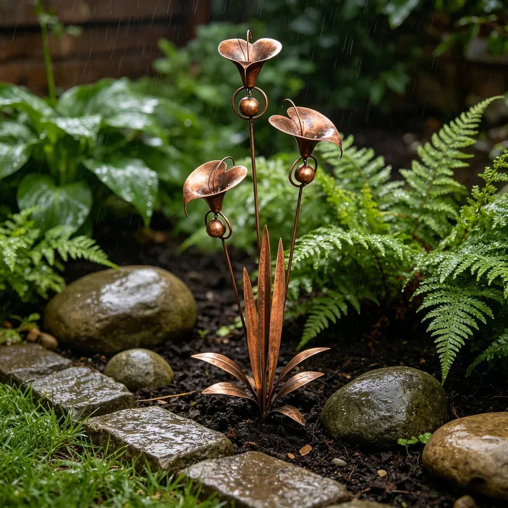 Tuteur décoratif en cuivre sous la pluie, entouré de fougères, de galets mouillés et de pavés, dans un coin de jardin ombragé. 3