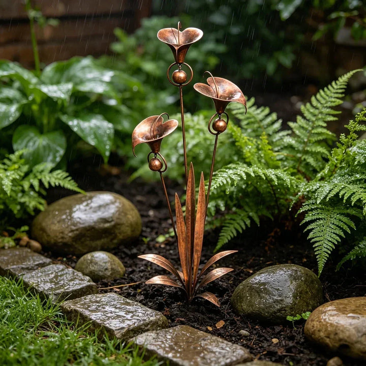 Tuteur décoratif en cuivre sous la pluie, entouré de fougères, de galets mouillés et de pavés, dans un coin de jardin ombragé. 3