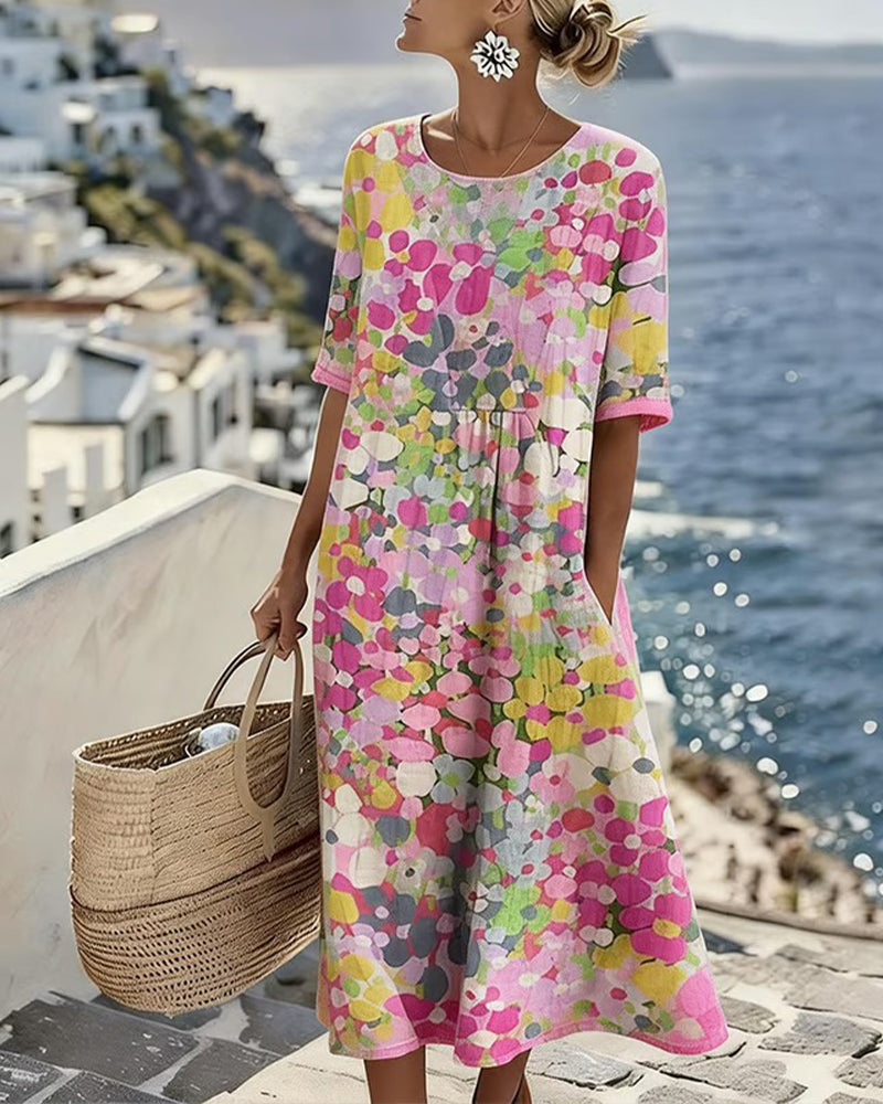 Robe à motif floral rose, jaune et vert portée en pied, une main dans la poche, panier de paille 1