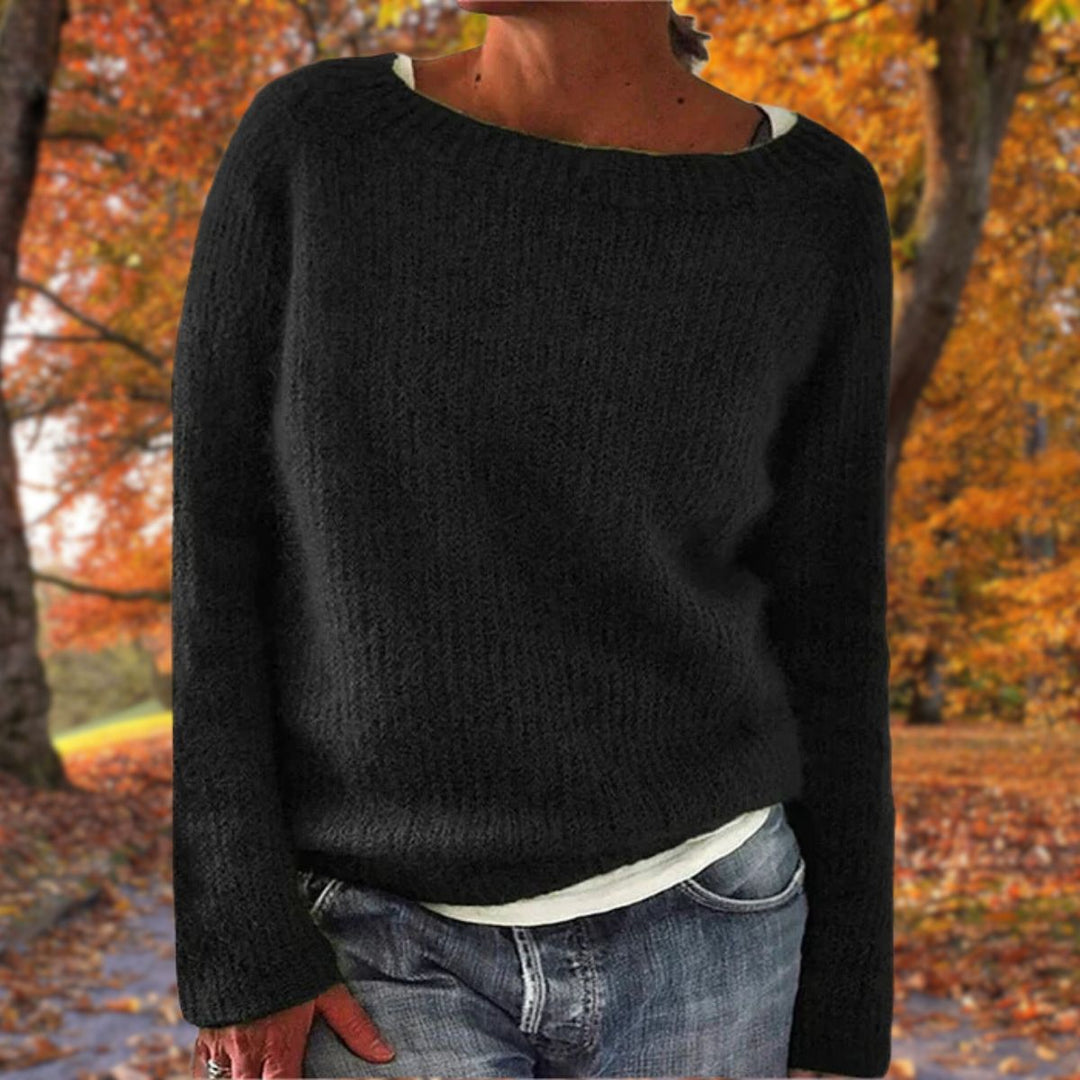 Pull en maille noir à col rond porté par une femme sur un t-shirt blanc, avec jean, dans un décor de forêt automnale. 2
