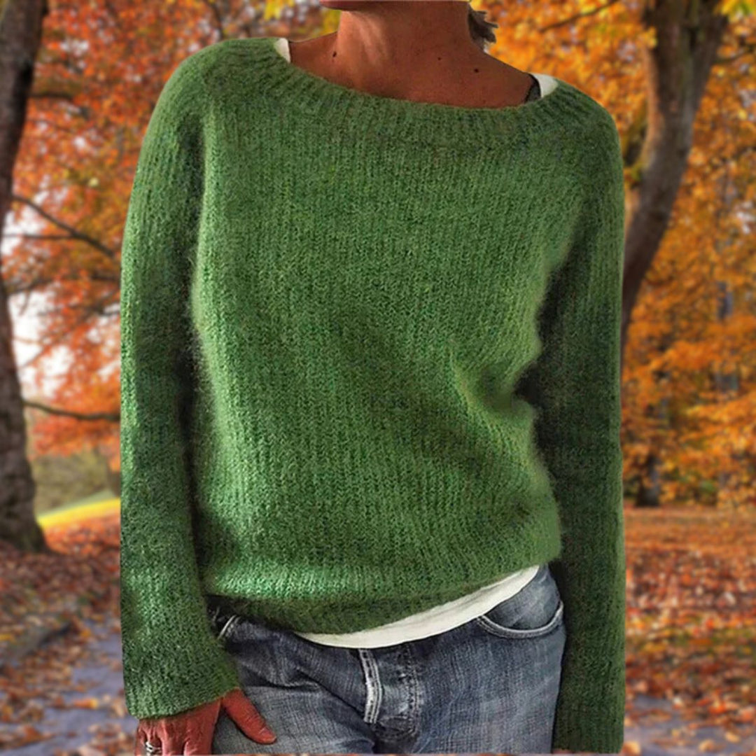 Pull en maille vert à col rond porté par une femme sur un t-shirt blanc, avec jean, devant des arbres d'automne. 5