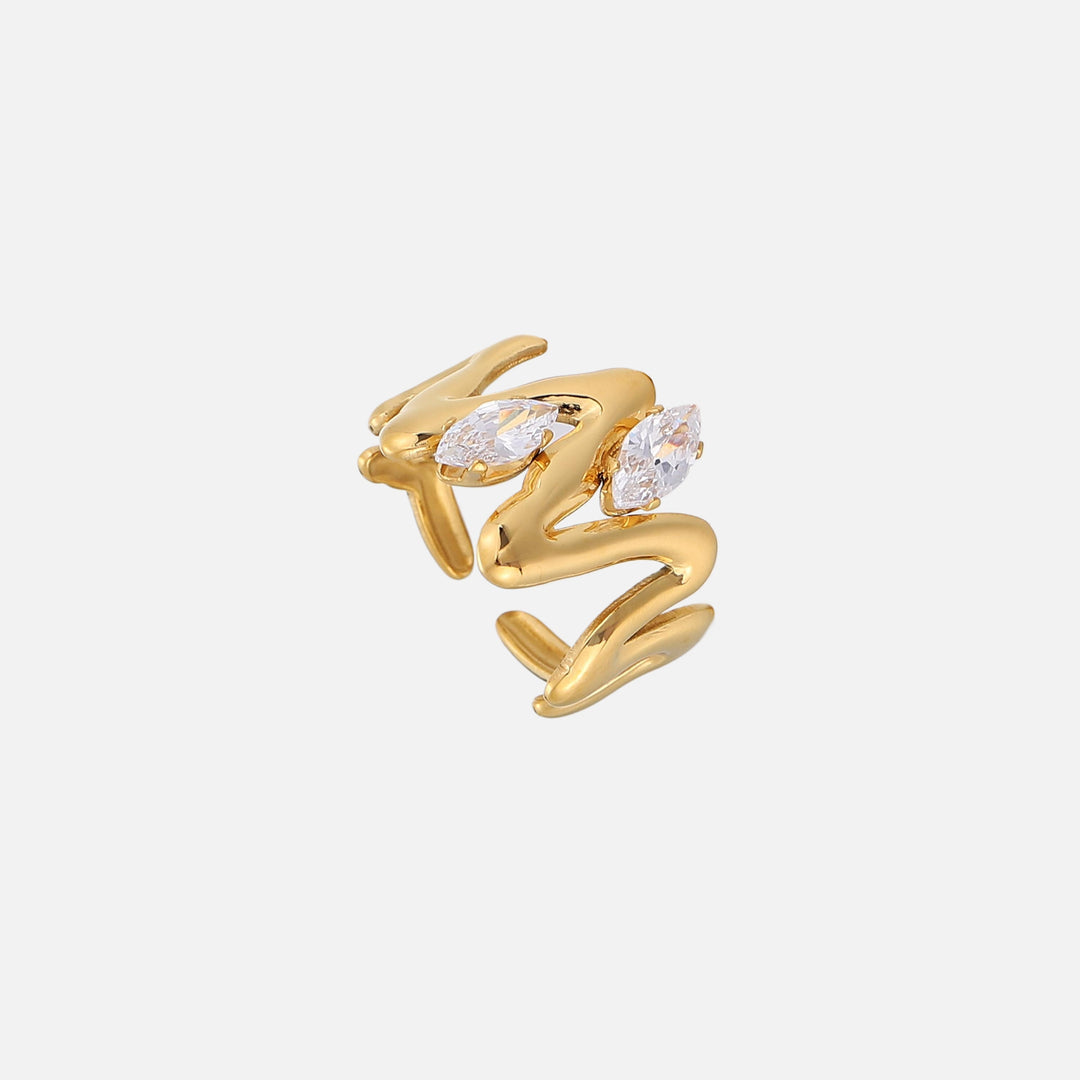 Bague dorée ouverte aux courbes fluides, vue de trois quarts, ornée de deux cristaux taille marquise sur fond clair uni. 1