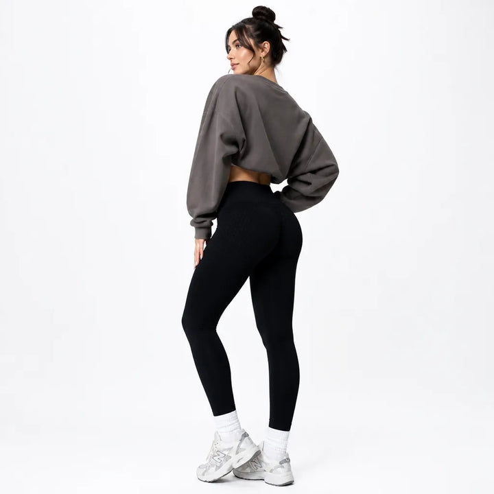 Legging noir taille haute porté de dos avec un sweat court gris foncé et des baskets blanches. 4