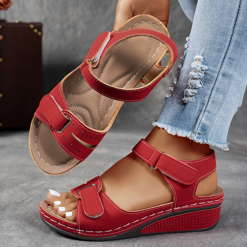 Sandales compensées rouges à brides auto-agrippantes et surpiqûres blanches, portées avec un jean déchiré, l'autre sandale montrant sa semelle matelassée. 2