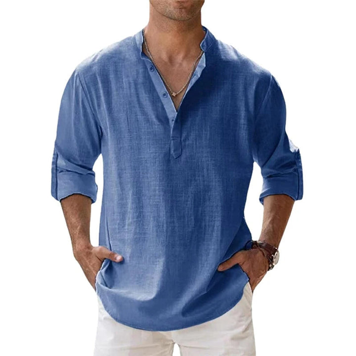 Homme portant la chemise Henley bleue, manches retroussées, mains dans les poches d'un pantalon blanc, vue de face. 2