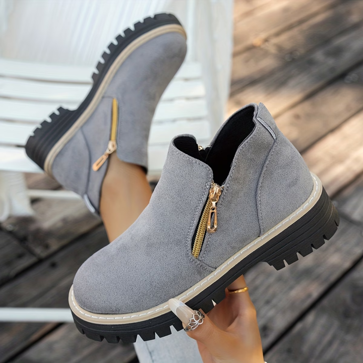 Bottines grises en suédine à semelle épaisse crantée et zip doré latéral, portées sur une terrasse en bois. 2