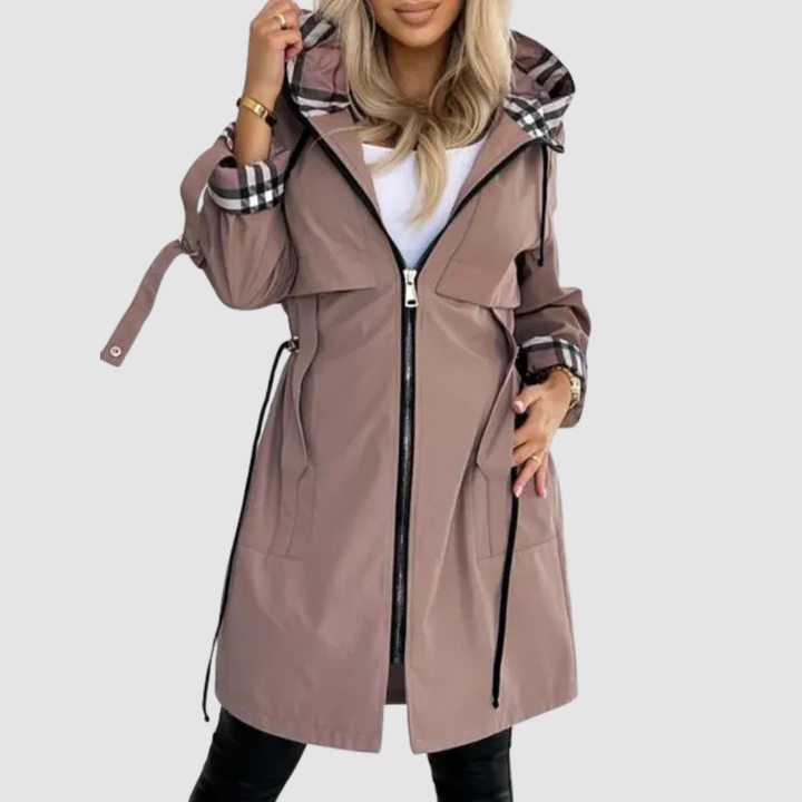 Femme portant le manteau taupe ouvert sur un haut blanc, doublure à carreaux visible à la capuche et aux poignets, lacets de taille. 1