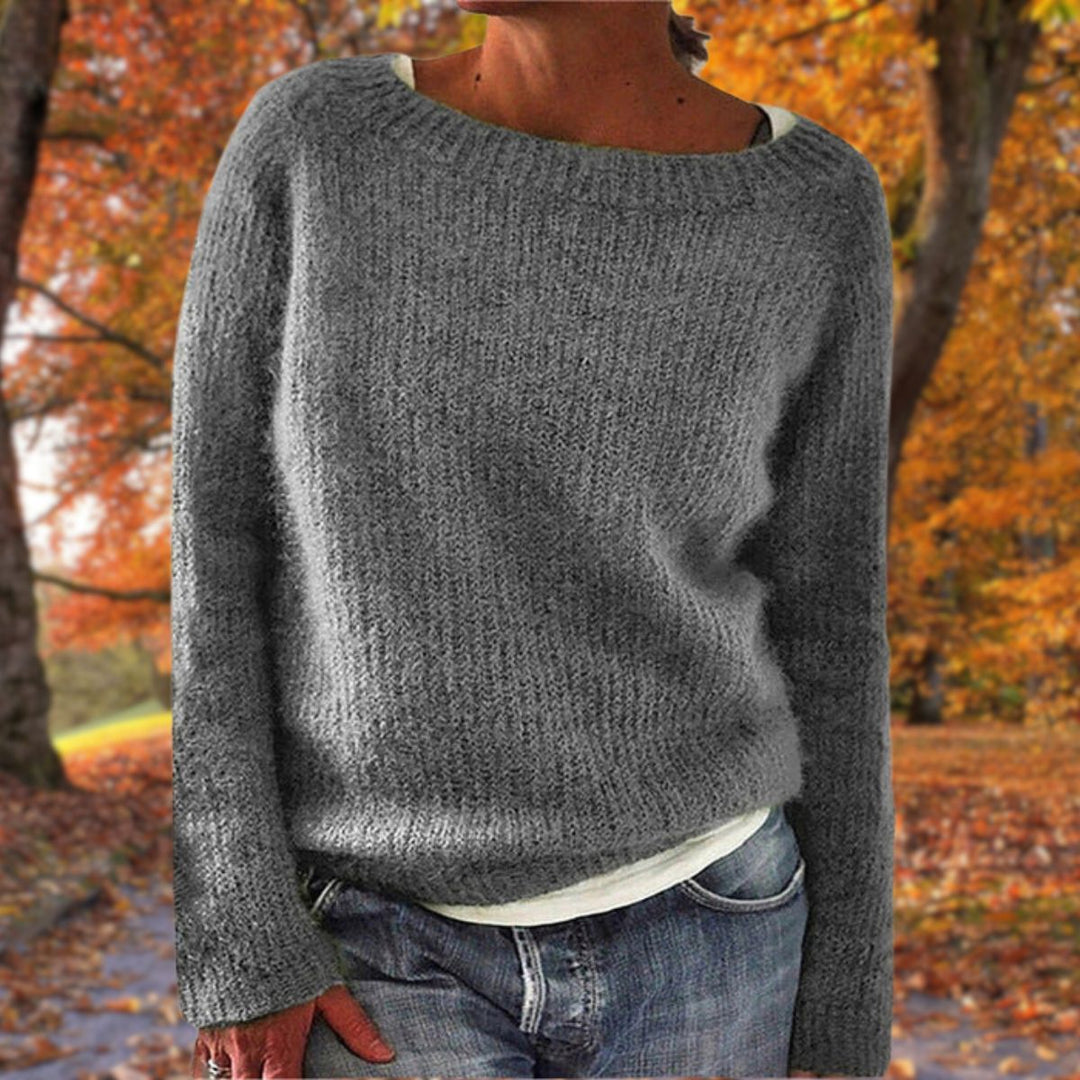 Pull en maille gris à col rond porté par une femme sur un t-shirt blanc, avec jean, dans un parc aux feuilles orangées. 4