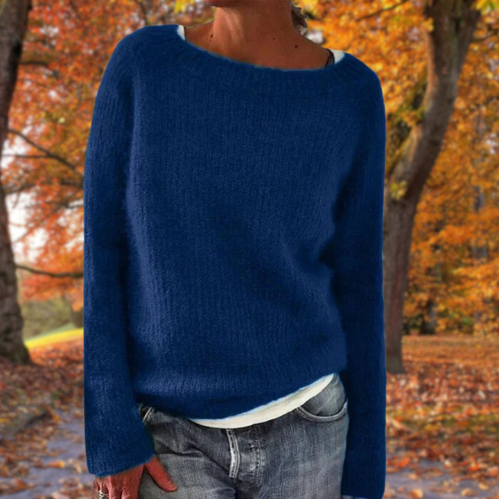 Pull en maille bleu marine à col rond porté par une femme sur un t-shirt blanc, avec jean, sous des arbres d'automne. 3