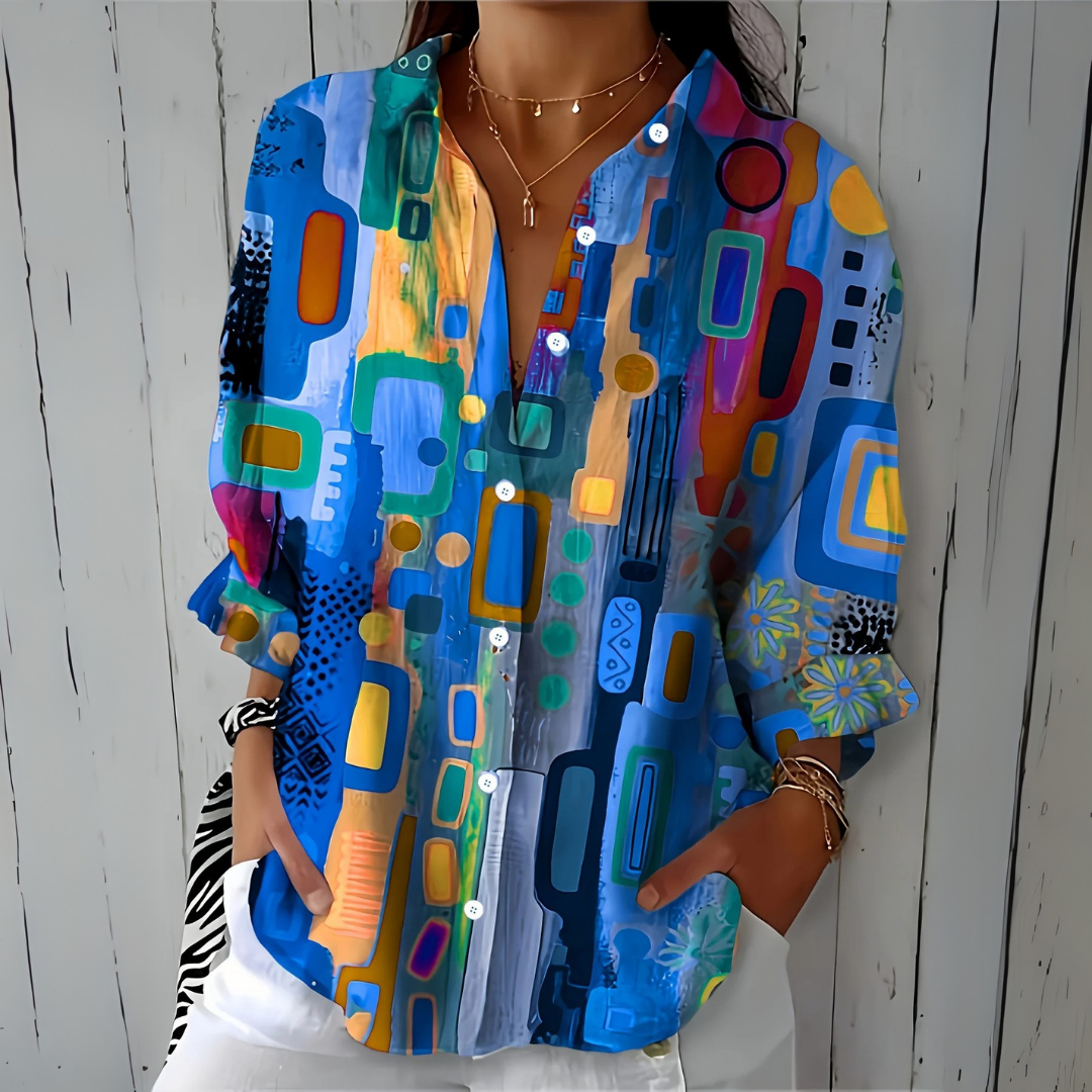 Blouse à motif abstrait dans les tons bleus, portée par une femme les mains dans les poches, pantalon blanc, vue de face. 1