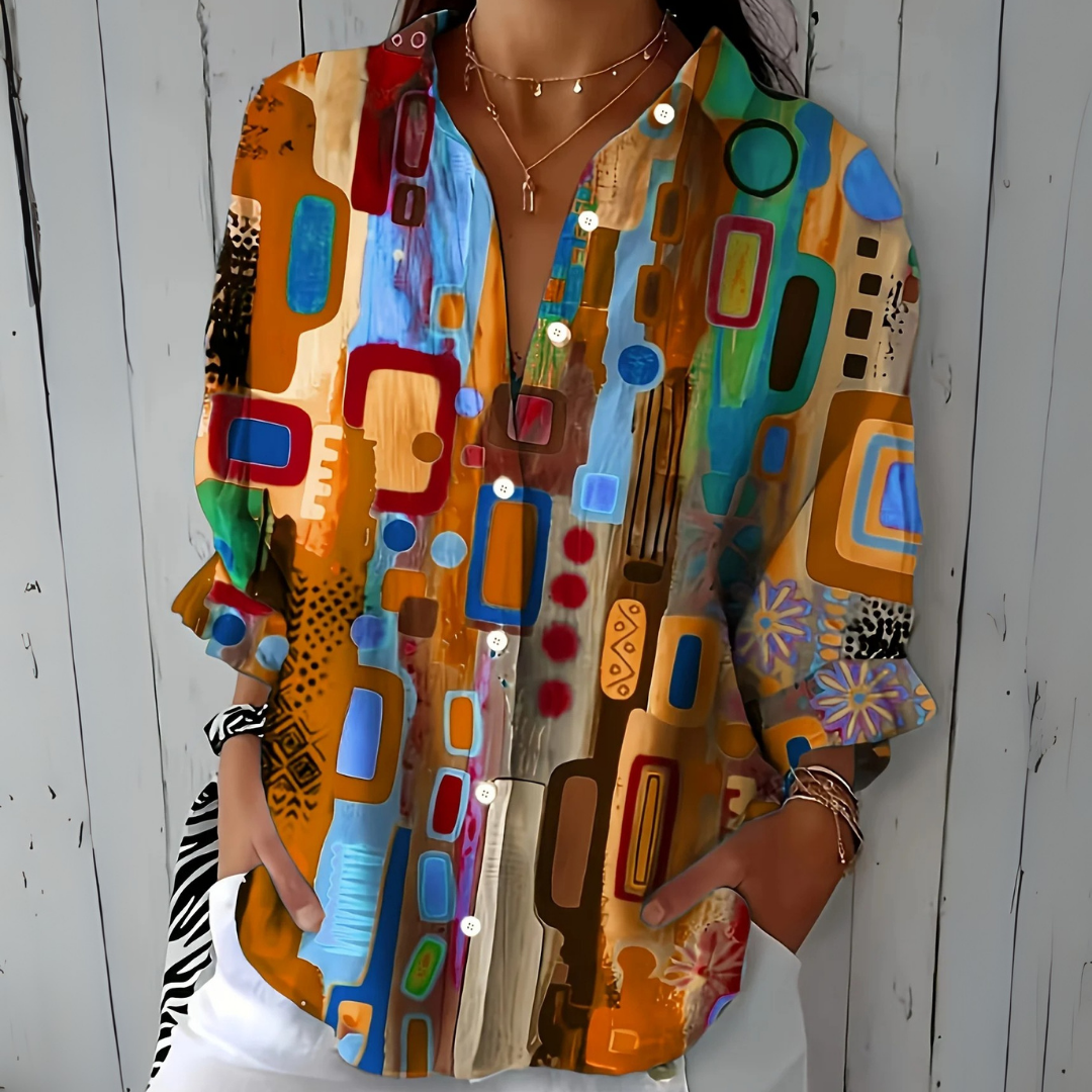 Blouse à motif abstrait aux tons orange, bleu clair et rouge, portée de face avec les mains dans les poches. 3