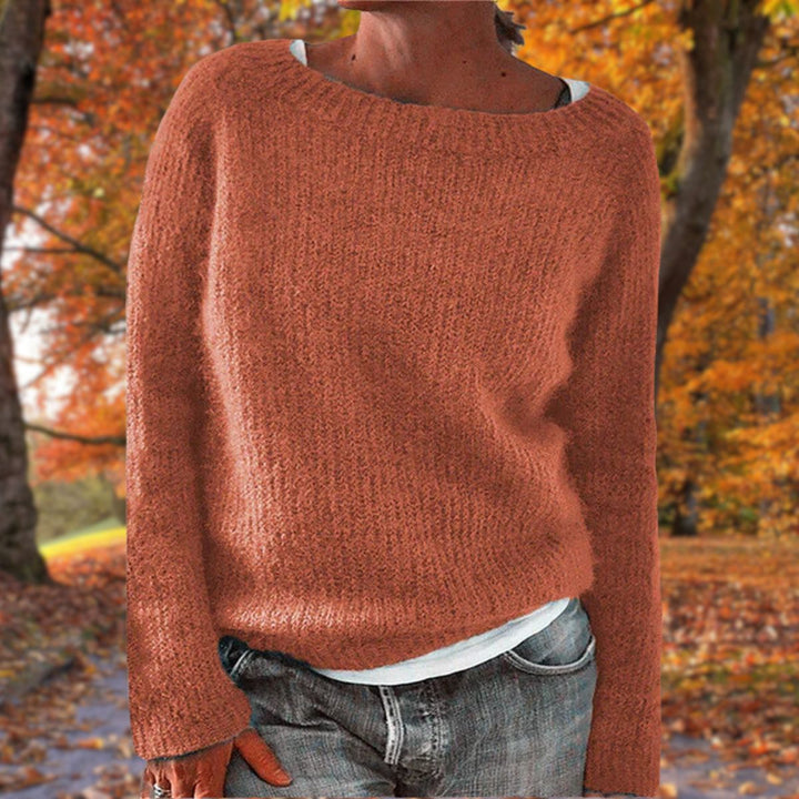 Pull en maille terracotta à col rond porté par une femme sur un t-shirt blanc, avec jean, dans un paysage d'automne. 6