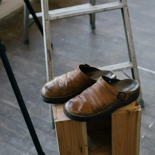 Paire de mules en cuir brun patiné posée sur un cube en bois, devant une échelle 1