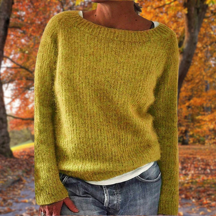 Pull en maille jaune moutarde à col rond porté par une femme sur un t-shirt blanc, avec jean, dans un parc d'automne. 1
