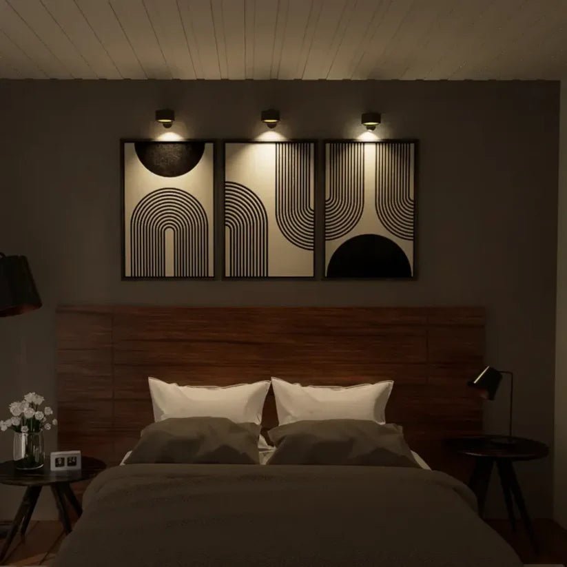 Trois appliques noires alignées au-dessus de trois tableaux graphiques, dans une chambre tamisée avec tête de lit en bois. 5