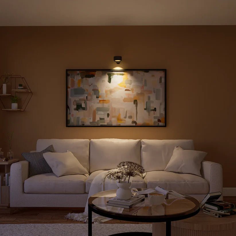 Applique noire éclairant un grand tableau abstrait au-dessus d'un canapé beige, dans un salon aux murs ocre. 8