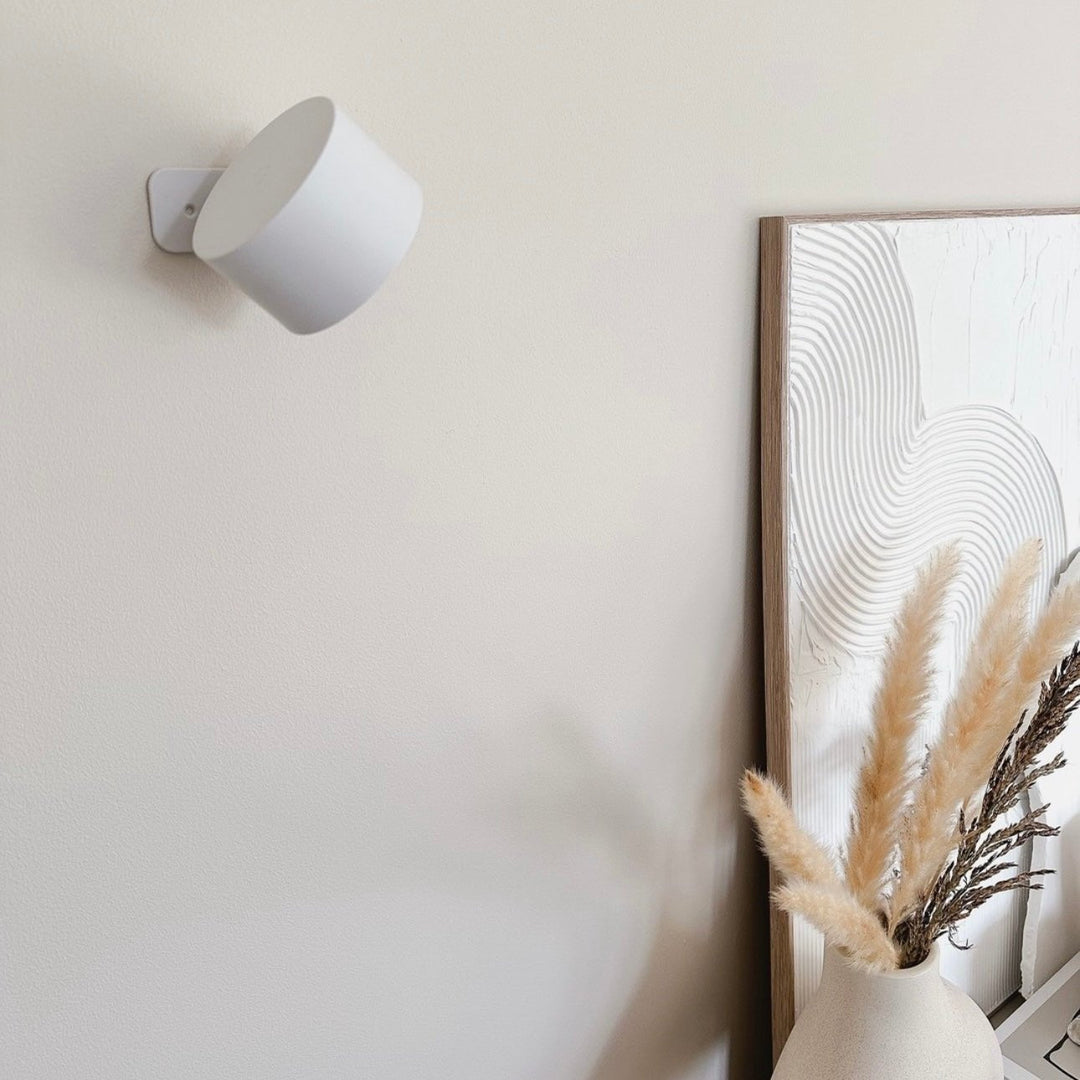 Applique blanche éteinte fixée à un mur beige, près d'un grand tableau texturé et d'un vase avec herbes de pampa. 17