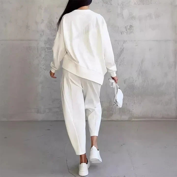 Vue de dos de l'ensemble blanc porté en marchant, avec ourlet du sweat asymétrique, pantalon ample et baskets blanches. 9