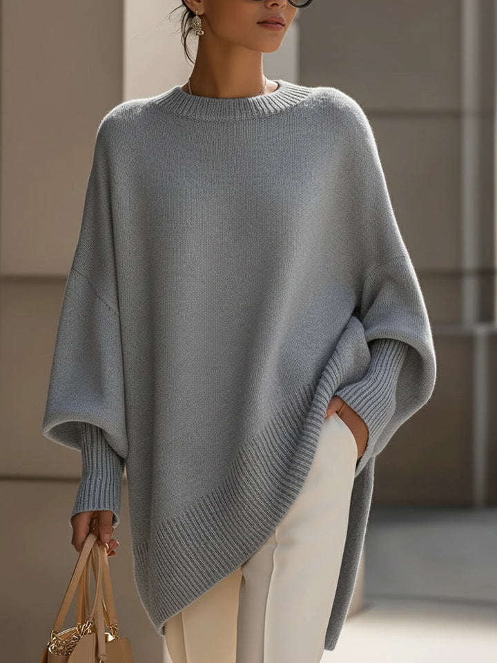 Poncho gris clair porté de face, ourlet côtelé asymétrique, pantalon blanc et sac 10
