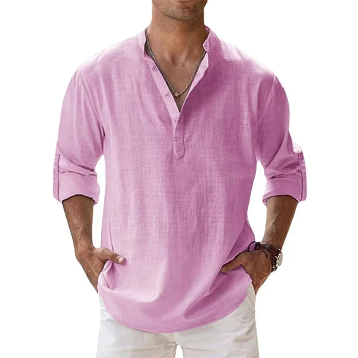 Homme portant la chemise Henley rose, manches retroussées, mains dans les poches d'un pantalon blanc, vue de face. 3