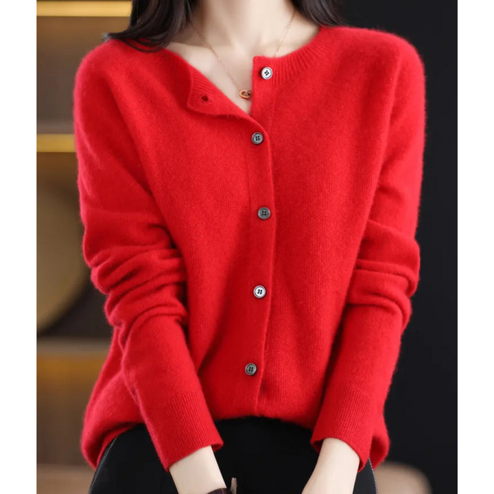 Cardigan rouge vif à col rond et boutons gris, porté avec un pantalon noir, mains posées sur les genoux. 14