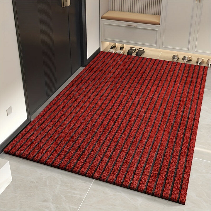 Même tapis à rayures en version rouge, posé sur un sol clair à côté d'une porte sombre et d'un meuble à chaussures. 2