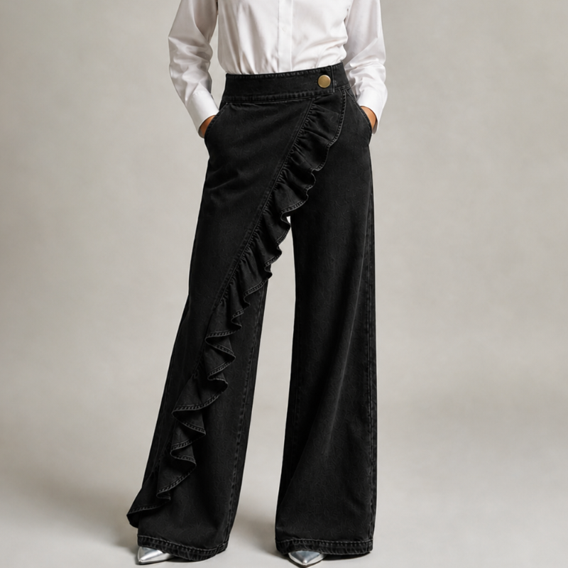 Vue de face en denim noir, mains dans les poches, chemise blanche, bouton doré et volant en diagonale sur la jambe large. 7