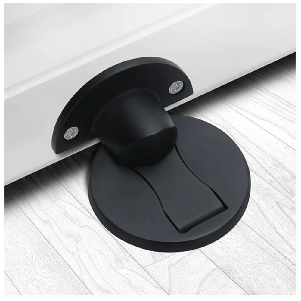 Version noir mat de la butée magnétique, vissée en bas d'une porte blanche au-dessus de son socle rond sur parquet. 2