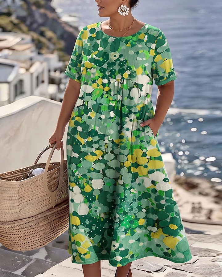 Robe verte et jaune portée par un mannequin en grande taille, main dans la poche, collier doré, vue sur la mer 6