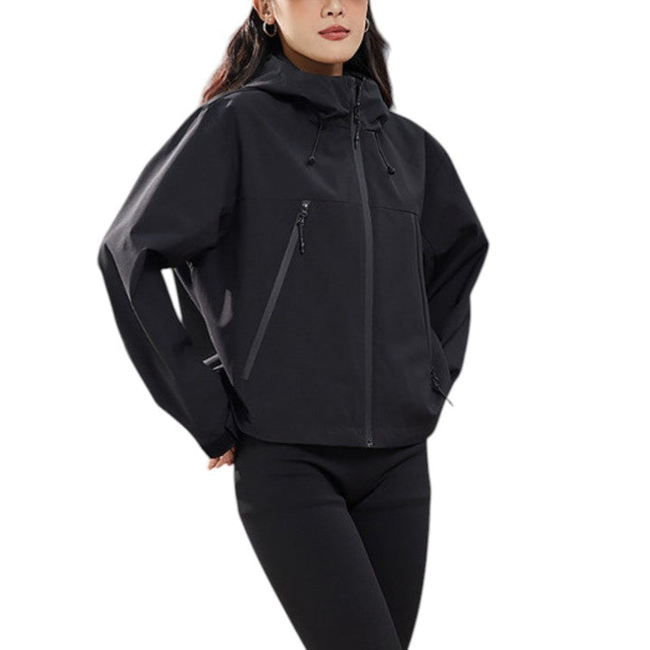 Plan rapproché de la veste noire portée, capuche avec cordons, poche zippée inclinée et ourlet droit, mains dans les poches. 17