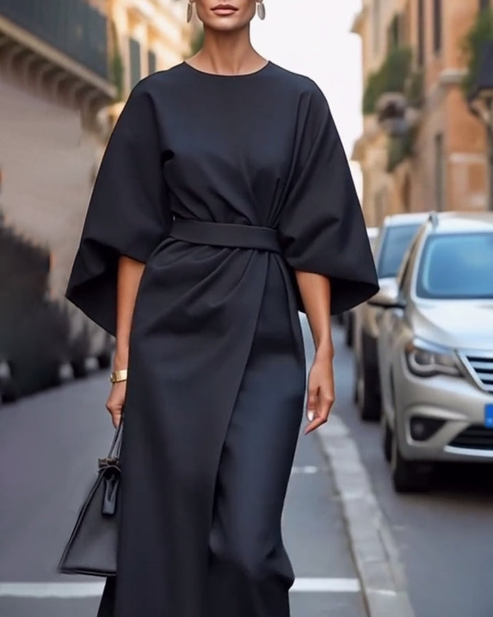 Robe noire drapée ceinturée aux manches évasées, portée dans une rue avec boucles d'oreilles et sac noir, cadrage resserré. 6