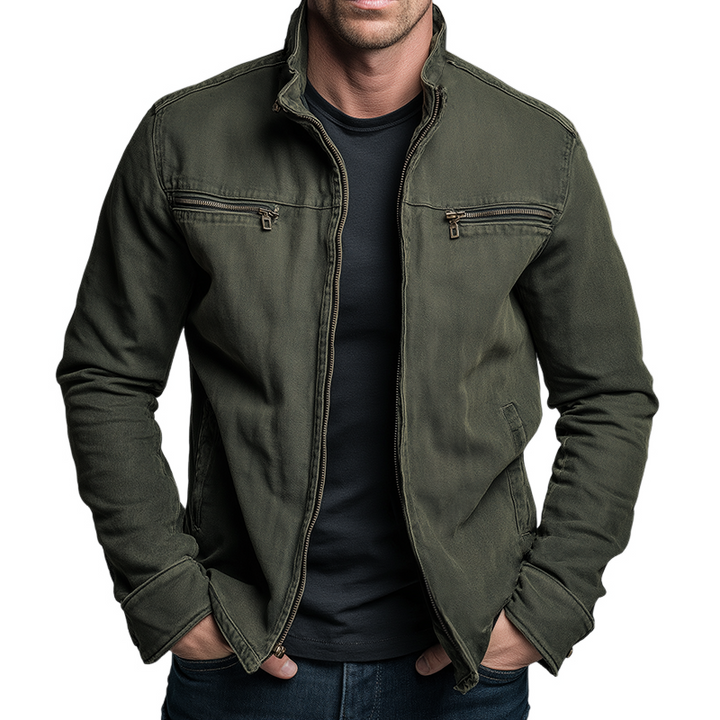 Veste verte à col montant, zippée sur un t-shirt noir, portée mains dans les poches, fond blanc 1