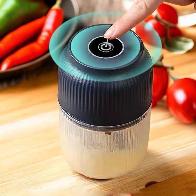 Gros plan sur le dessus du hachoir bleu foncé, un doigt appuyant sur le bouton marche-arrêt, avec piments et tomates en arrière-plan. 2