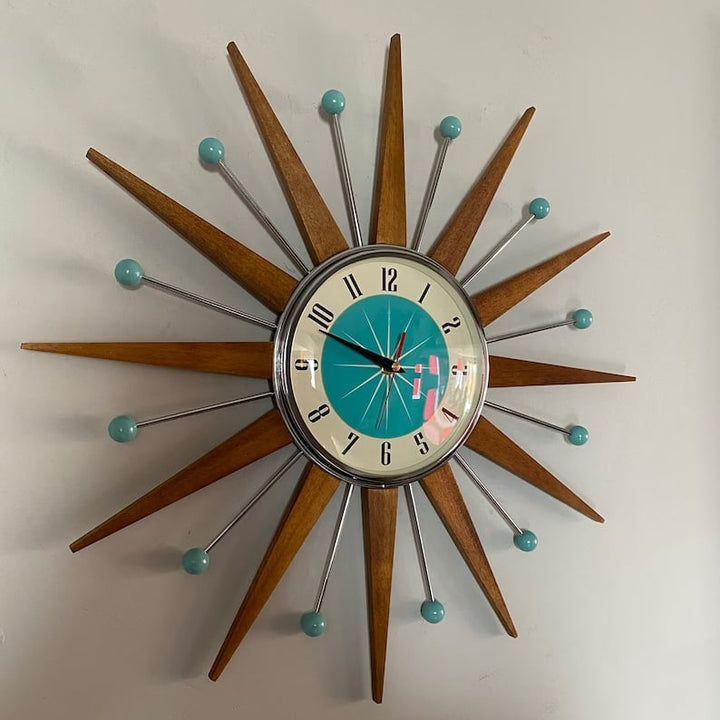 Horloge soleil accrochée à un mur gris clair, vue de face, rayons en bois et boules turquoise au bout des tiges. 2