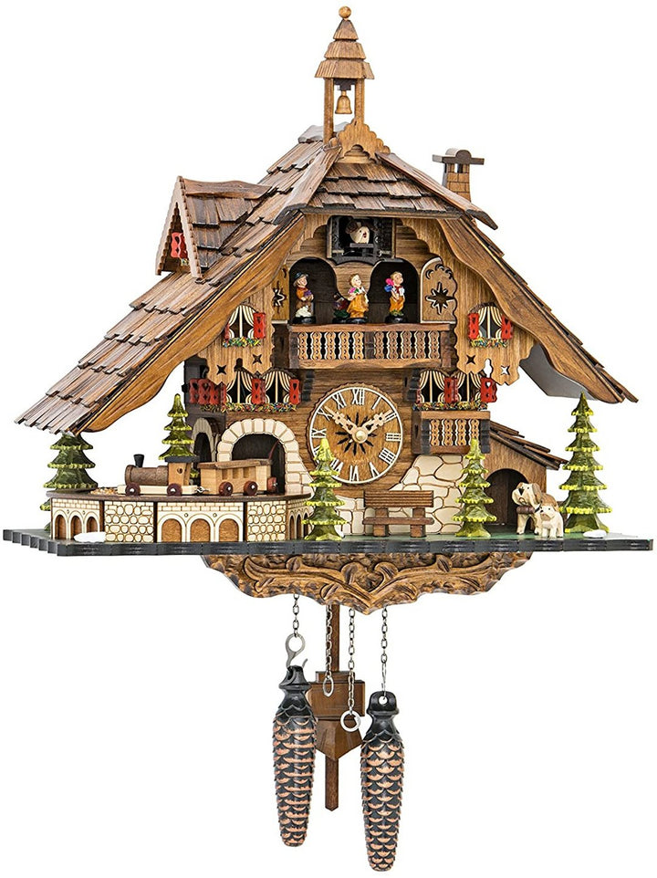 Grand chalet en bois sculpté avec toit de bardeaux, clocheton, petit train, sapins, chiens et personnages sur le balcon. 1