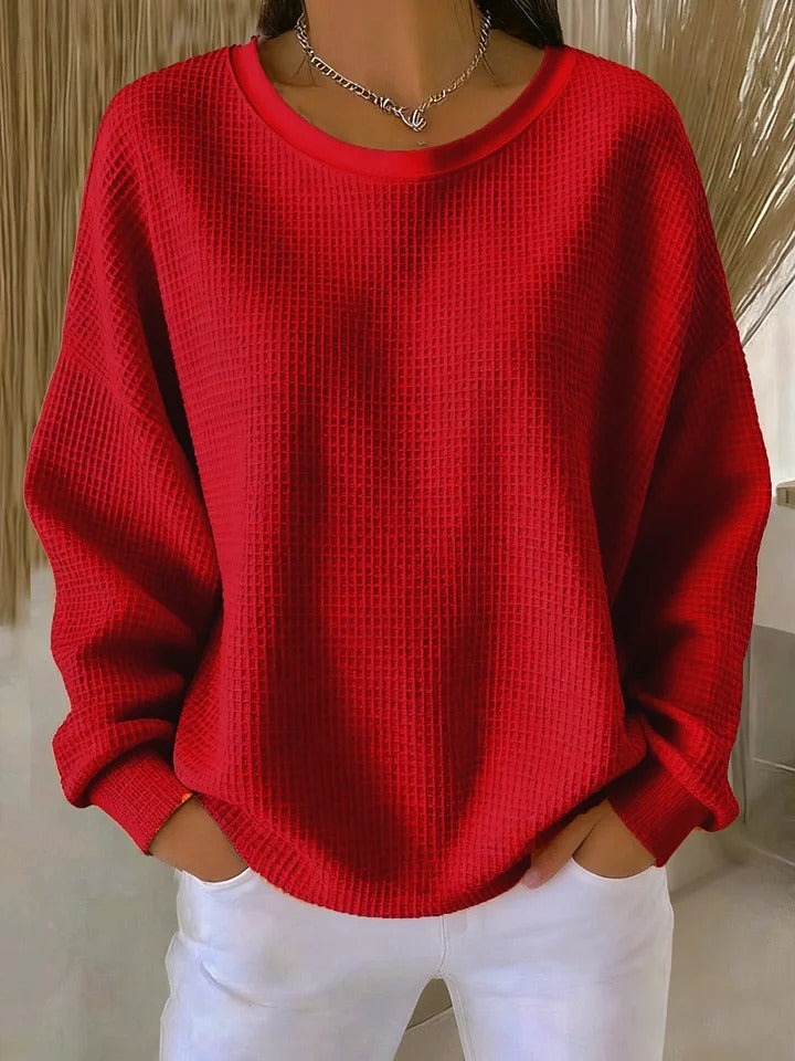 Pull gaufré rouge à col rond et manches longues, porté par un modèle, les mains dans les poches d'un pantalon blanc. 2