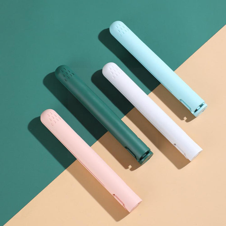 Quatre lisseurs fermés, bleu clair, blanc, vert foncé et rose, alignés en diagonale sur un fond bicolore vert et beige. 5