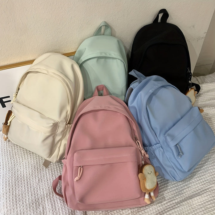 Cinq sacs à dos beige, vert menthe, noir, rose et bleu posés ensemble sur un lit, avec porte-clés en forme de toast. 8