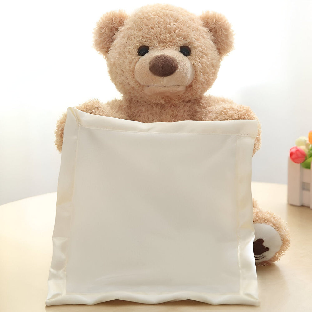 Ours en peluche beige vu de face, les bras levés tenant devant lui un carré de tissu crème, posé sur une table. 2