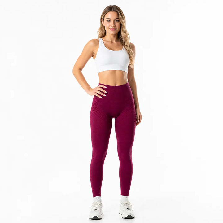 Femme de face en legging bordeaux taille haute avec fines lignes texturées sur les hanches, brassière blanche, main sur la hanche. 15