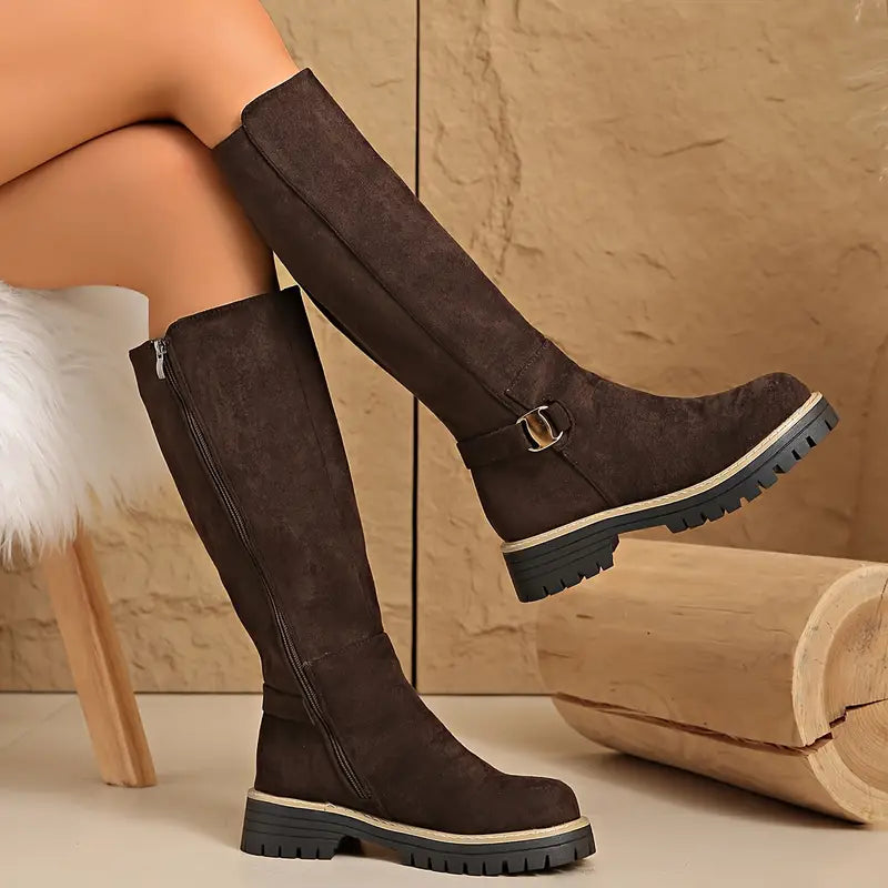 Bottes hautes marron foncé en effet daim portées jambes croisées, avec fermeture éclair latérale et semelle noire crantée. 5