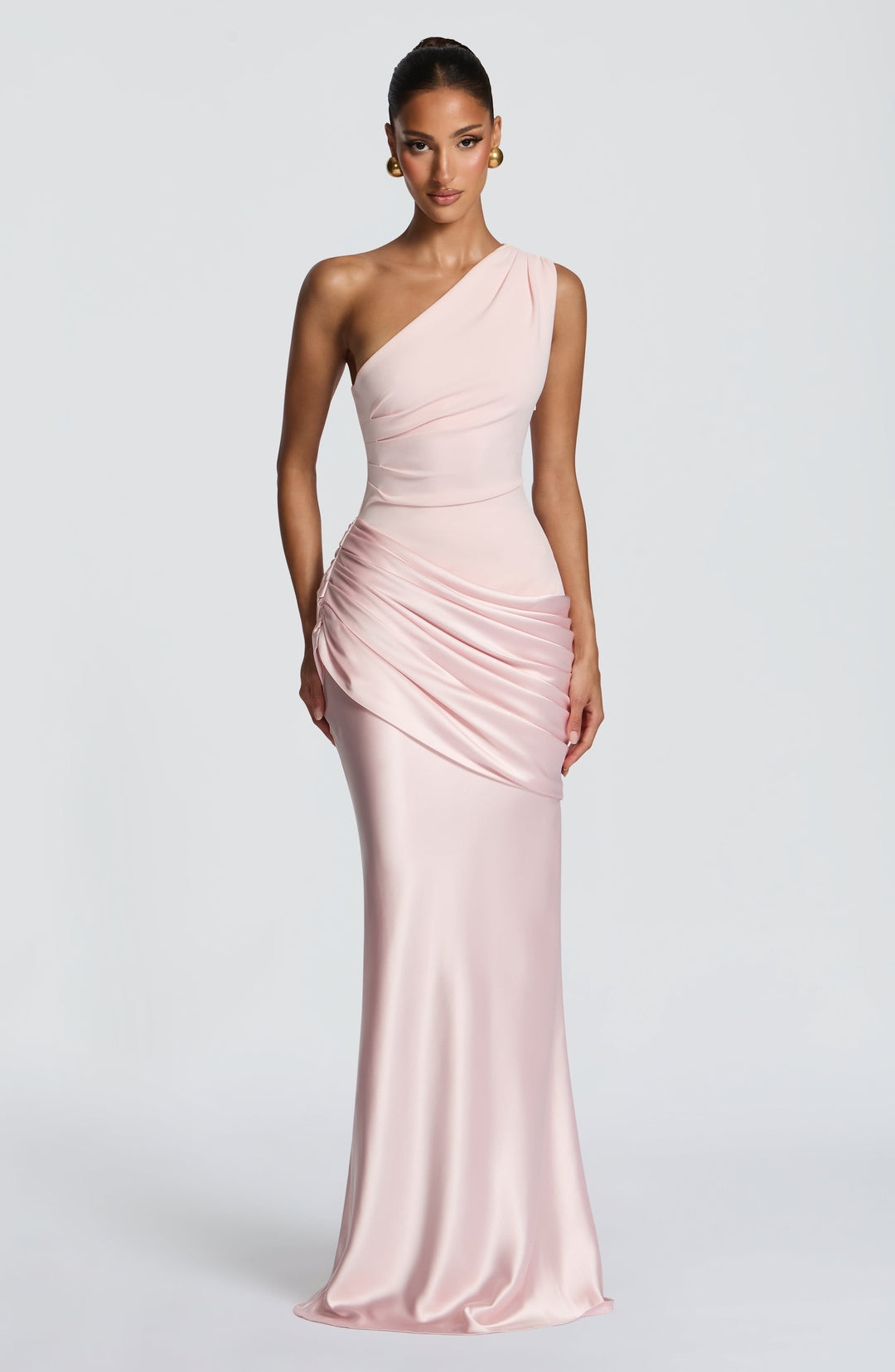 Robe longue rose pâle portée de face, haut asymétrique plissé, drapé en satin sur la hanche, boucles d'oreilles dorées. 11