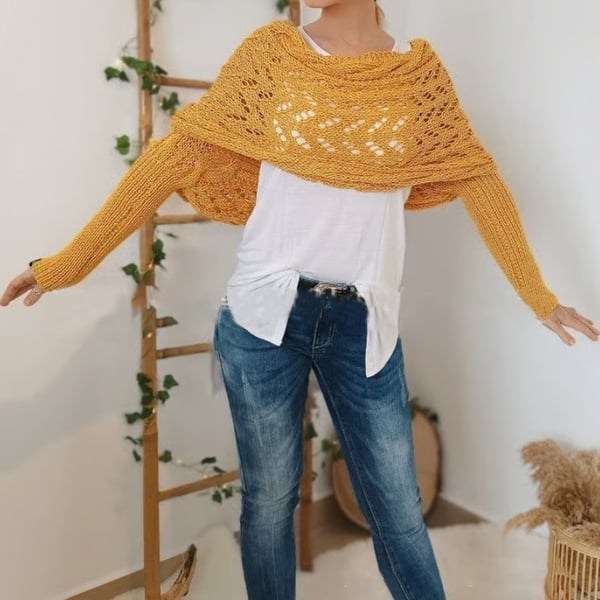 Châle ajouré jaune moutarde à manches intégrées porté bras écartés, sur un t-shirt blanc et un jean, devant une échelle décorative. 22