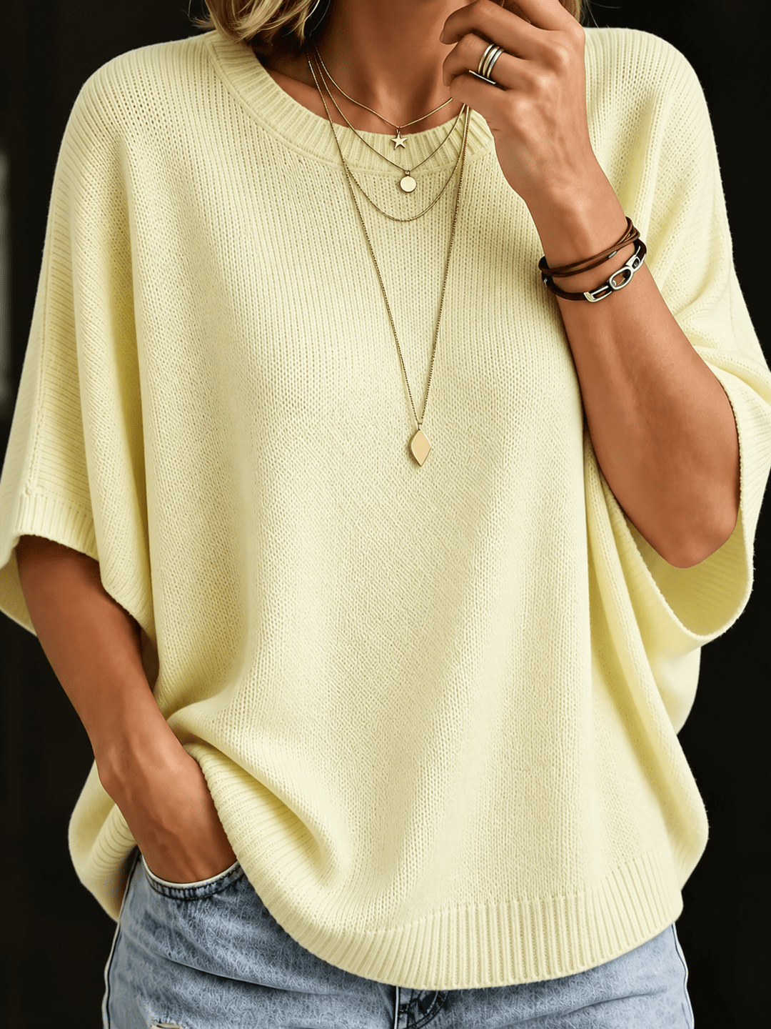 Top en maille jaune pâle, plan rapproché de face, col rond côtelé, manches amples, colliers superposés et bracelets en cuir. 4