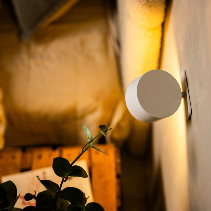 Dos de l'applique blanche vu de côté, avec le bouton tactile rond sur le capot et le support fixé au mur. 13