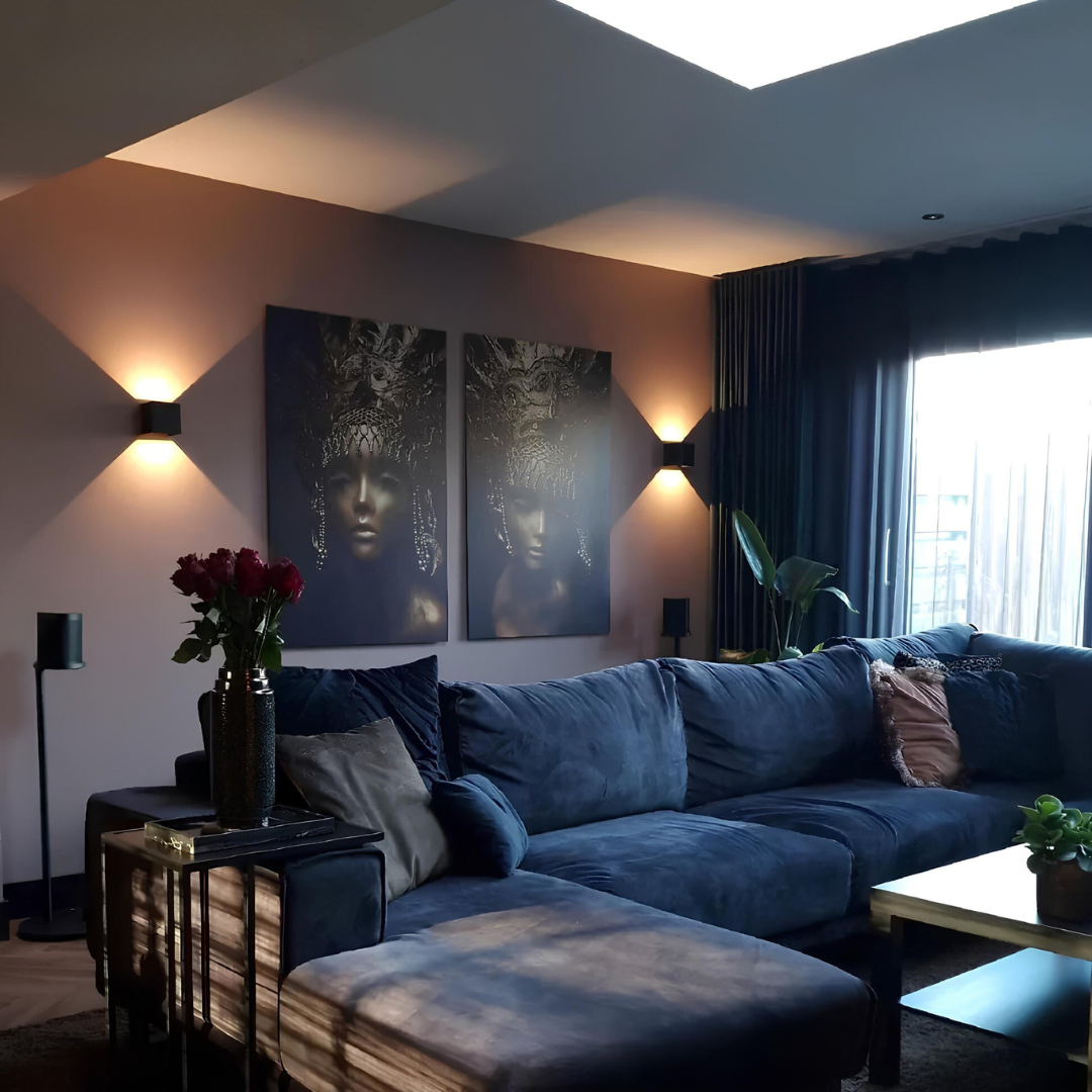 Deux appliques cubiques noires de part et d'autre de deux tableaux, dans un salon avec grand canapé bleu et rideaux sombres. 9