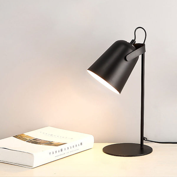 Version noire de la lampe allumée, posée sur un plan clair à côté d'un livre, abat-jour incliné vers la gauche. 12