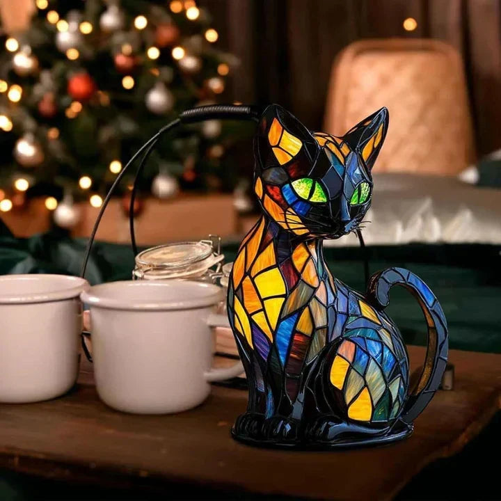 Chat vitrail posé sur une table en bois près de deux tasses blanches, sapin illuminé derrière 3