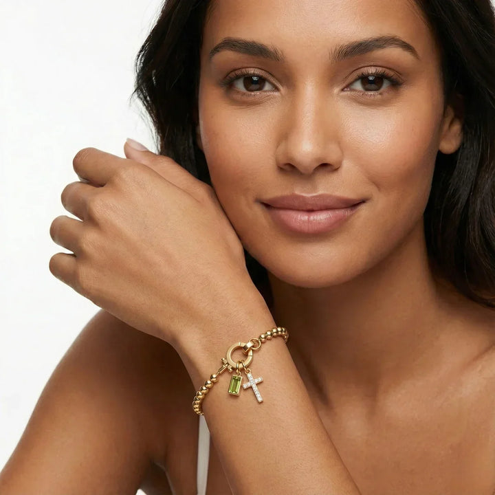 Portrait d'une femme souriante, main près du visage, portant le bracelet doré à perles avec croix et pierre verte. 12