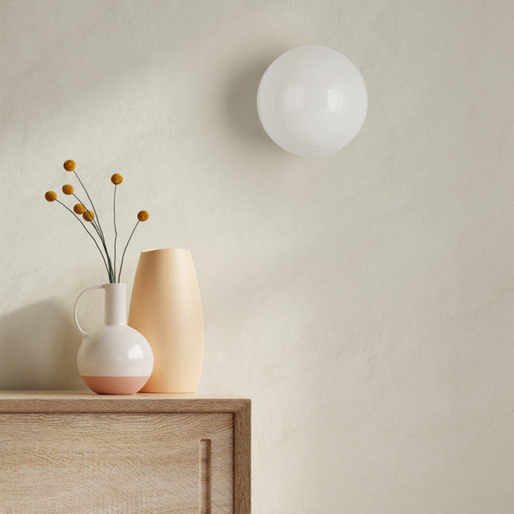 Sphère en verre blanc brillant accrochée au mur, éteinte, près d'un meuble et de vases 6